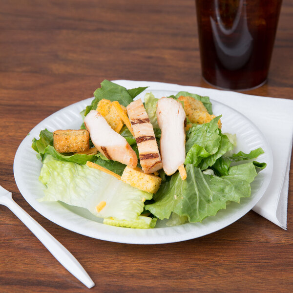 A Dart white foam plate with salad, chicken, and lettuce on it.