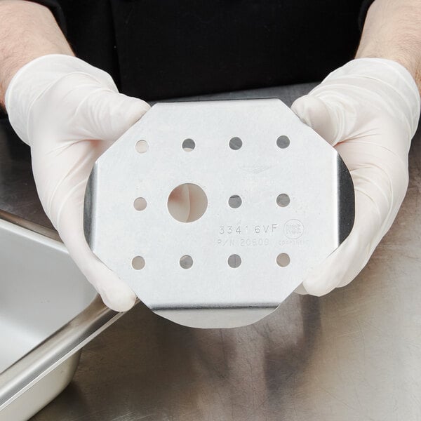 A person in white gloves holding a Vollrath stainless steel false bottom.