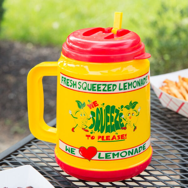 A yellow "We Squeeze to Please" pitcher with a red lid and straw on a table.