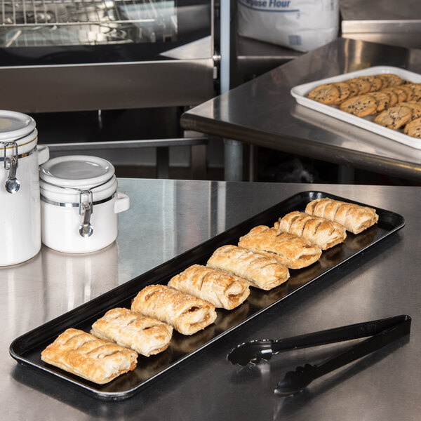 A black Carlisle fiberglass market tray holding pastries on a counter.