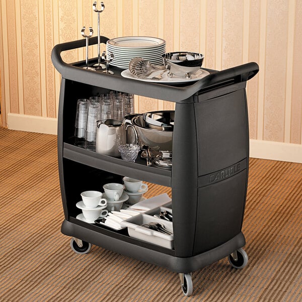 A black Carlisle utility cart with a shelf of dishes.