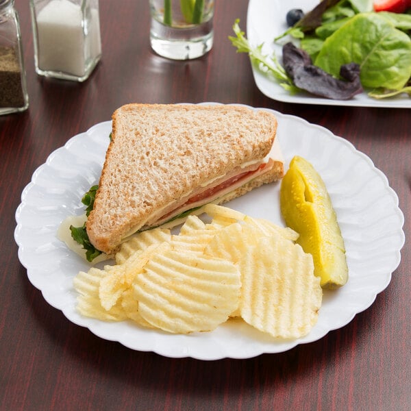 A Fineline Flairware white plastic plate with a sandwich and chips on it.