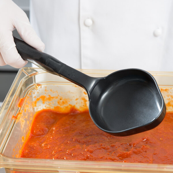 A gloved hand using a black Vollrath Spoodle to serve red sauce.