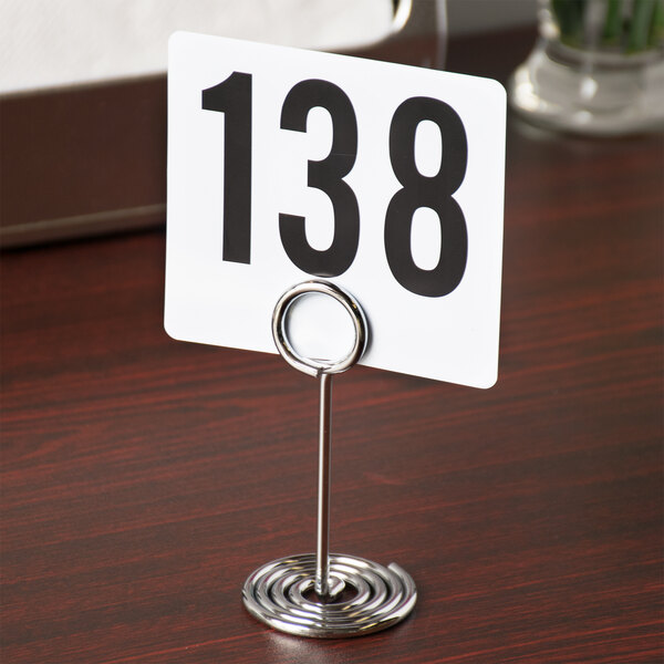 An American Metalcraft chrome swirl base table card holder with a white sign and black numbers on it.