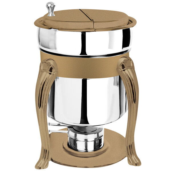 A stainless steel Queen Anne soup marmite with bronze accents and fuel holder on a table outdoors.