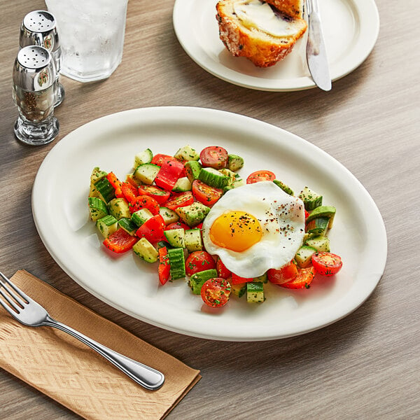 An Acopa narrow rim oval stoneware platter with food on it, on a table in a breakfast diner.