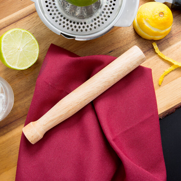 A Tablecraft natural wood muddler with lemons and limes on a table.