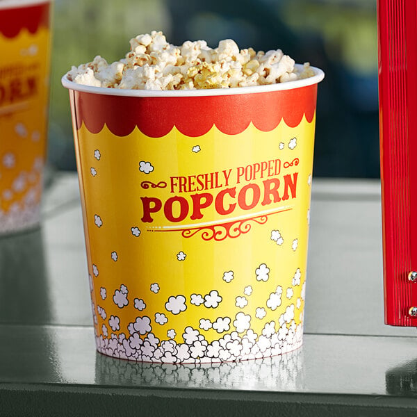 A yellow Carnival King popcorn bucket on a table filled with popcorn with a red and white label.