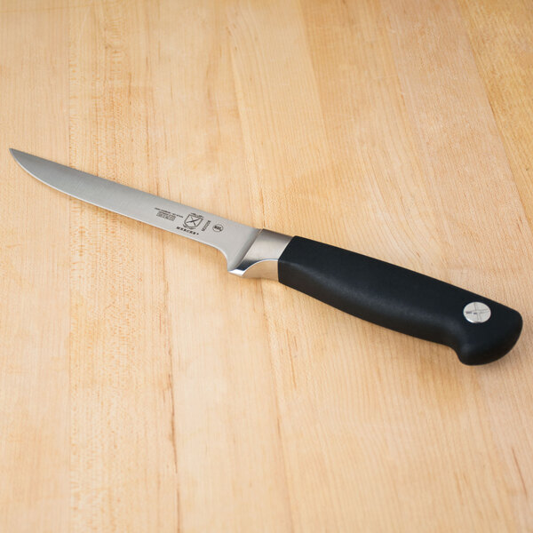 A Mercer Culinary Genesis flexible boning knife with a black handle on a wooden table.