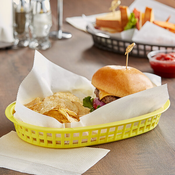 A yellow Tablecraft oval platter basket with a burger and chips in it.