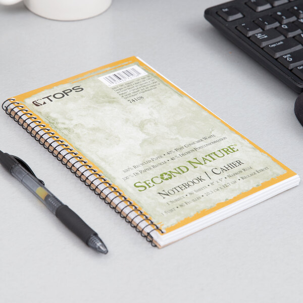 A TOPS Second Nature narrow ruled notebook with a green cover and pen on a table.