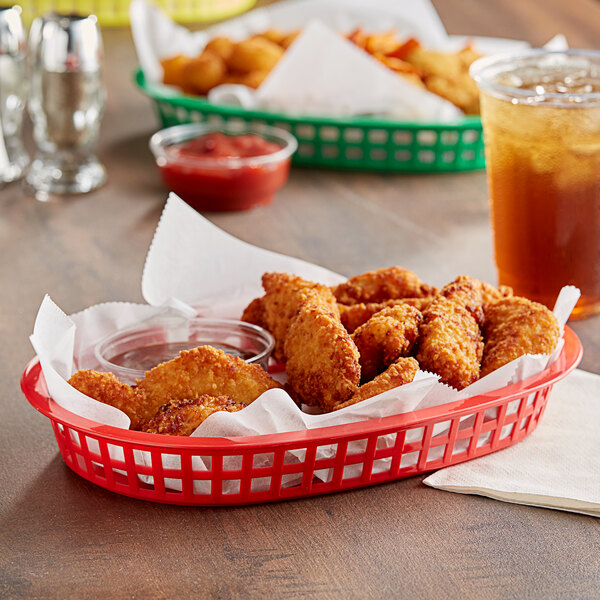 A Tablecraft red oval platter basket filled with fried chicken and a drink on a table.