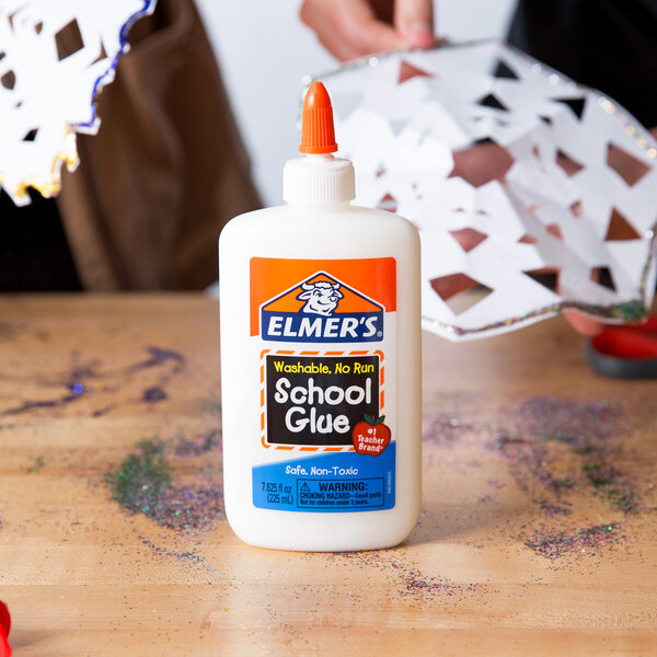 A person holding a white bottle of Elmer's school glue on a table.