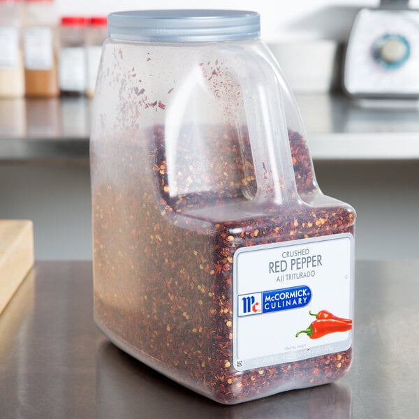 A large container of McCormick Culinary Crushed Red Pepper on a white counter.