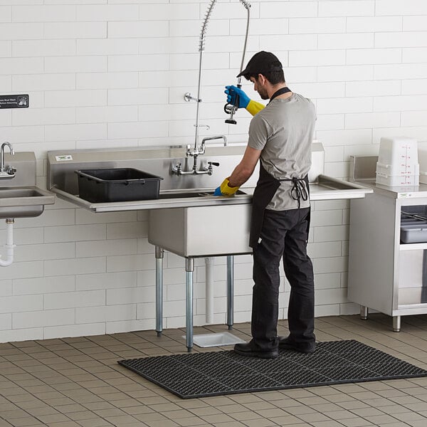 A man cleaning a Regency stainless steel one compartment sink in a professional kitchen.
