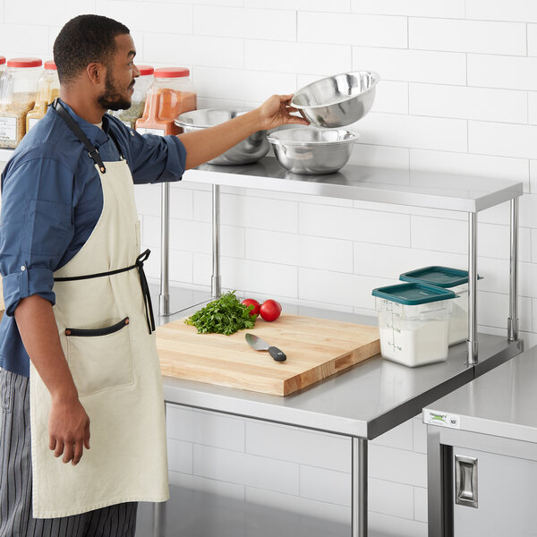 A man in a white apron using a Regency stainless steel table mounted overshelf.