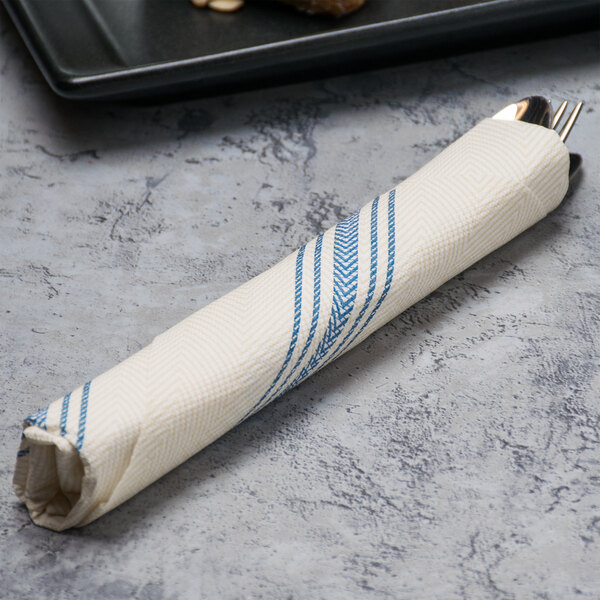 A Hoffmaster FashnPoint white napkin with blue dishtowel print on a table with a fork and knife.