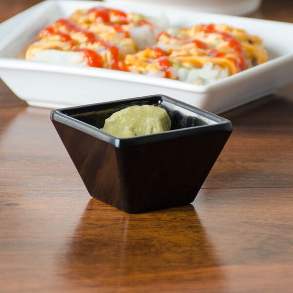 An American Metalcraft black square sauce cup with green sauce on a table.