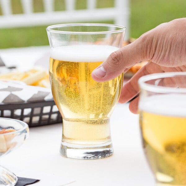 A hand holding a Libbey Stackable Craft Beer Glass filled with beer on a table in a bar.
