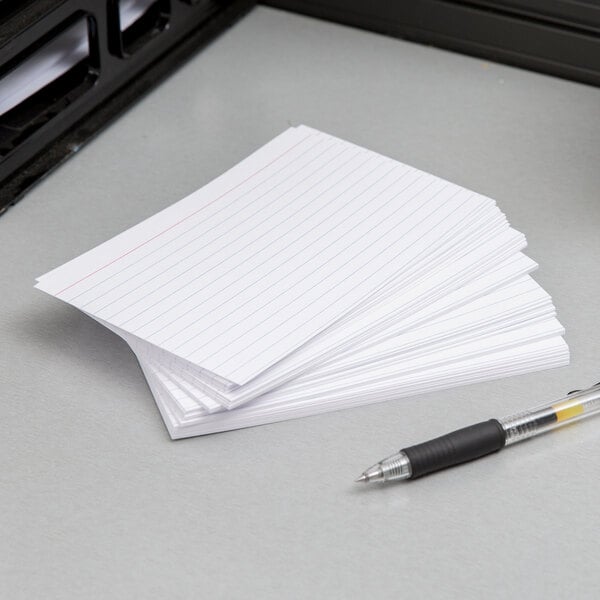 A stack of Oxford white ruled index cards next to a black and silver pen on a desk.