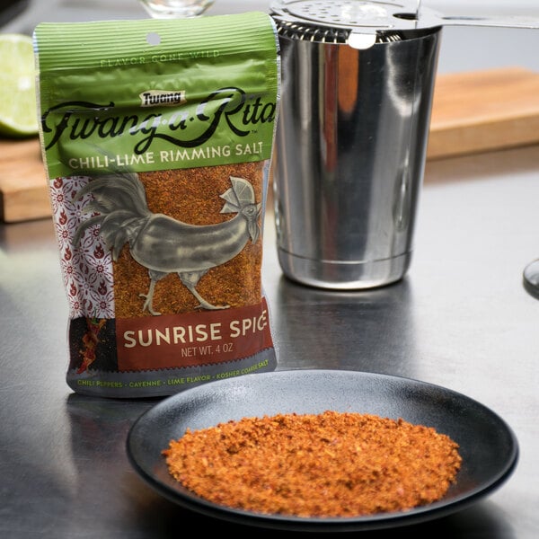 A bowl of Twang-a-Rita Sunrise Spice Chili-Lime Rimming Salt next to a bag of chili powder.