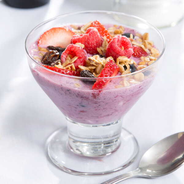 A Libbey dessert glass filled with fruit and oatmeal with a spoon in it.
