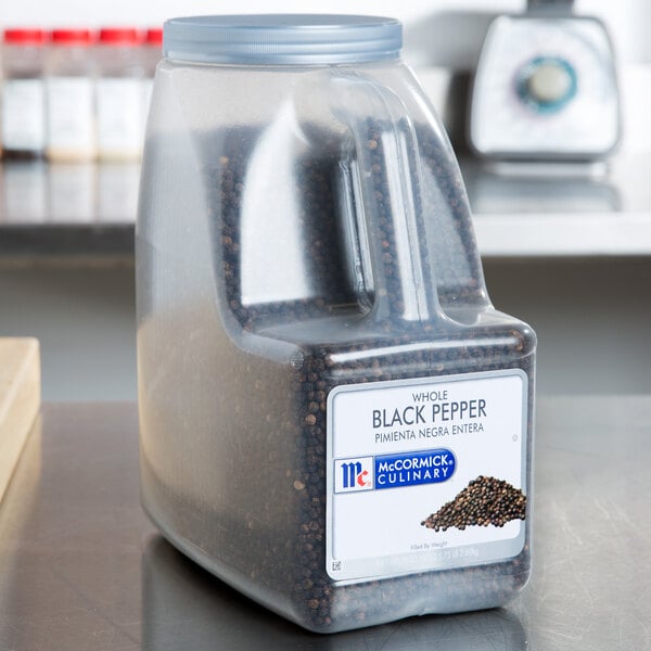 A plastic container of McCormick Culinary Whole Black Pepper on a counter.