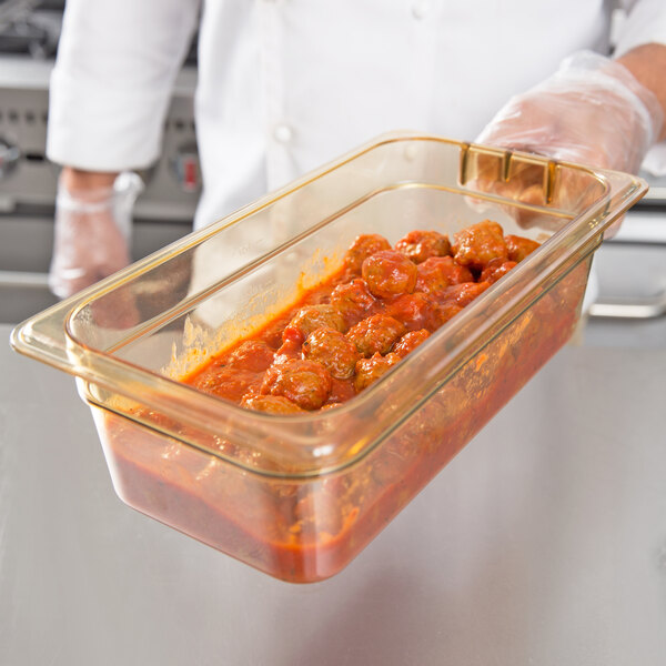 A person holding a Carlisle amber plastic food pan with meatballs in it.