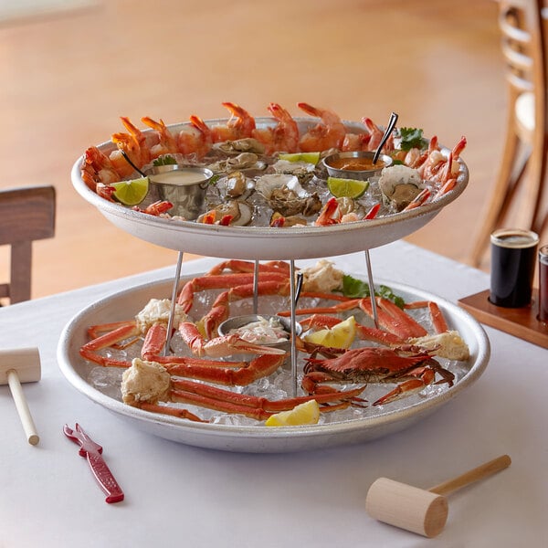 A two tiered seafood tower with large aluminum trays and stand holding seafood on a table.