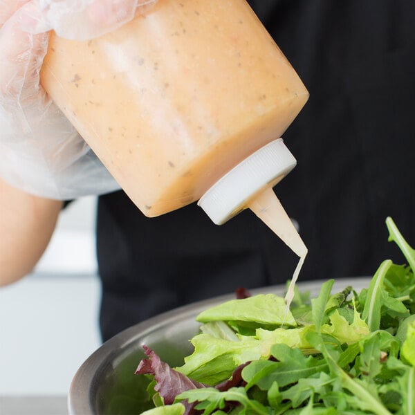 A person pouring Tablecraft clear sauce from a squeeze bottle into a bowl of salad.