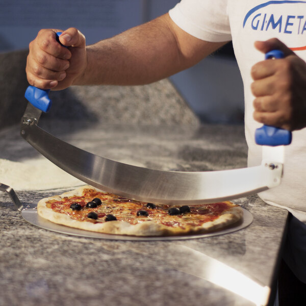 A person using a GI Metal stainless steel pizza rocker knife to cut a pizza.