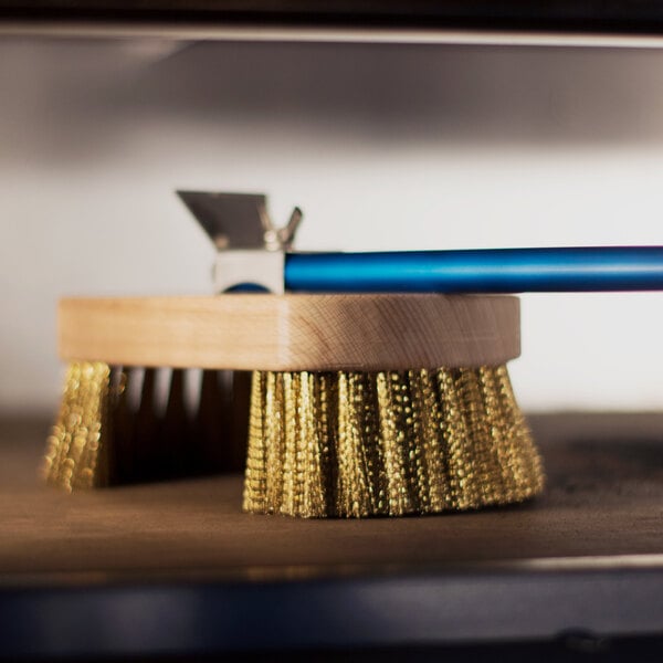 A GI Metal round pizza oven brush with a brass swivel head and a blue handle on a wooden surface.