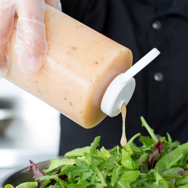 A person pouring sauce from a Tablecraft squeeze bottle onto a salad.