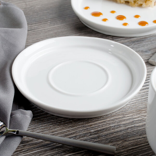 A white Bon Chef porcelain saucer on a wood table with a spoon on it.
