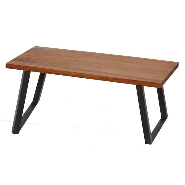 A walnut wood riser with foldable black metal legs on a wooden table.