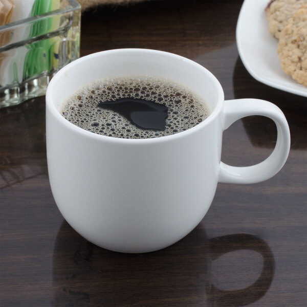 A white Bon Chef porcelain cup filled with a brown liquid sitting on a table.