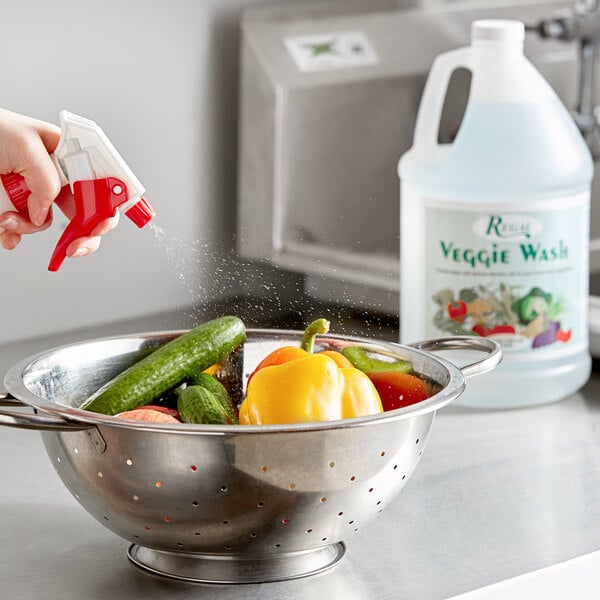 A hand using Regal Veggie Wash to spray a bowl of vegetables.