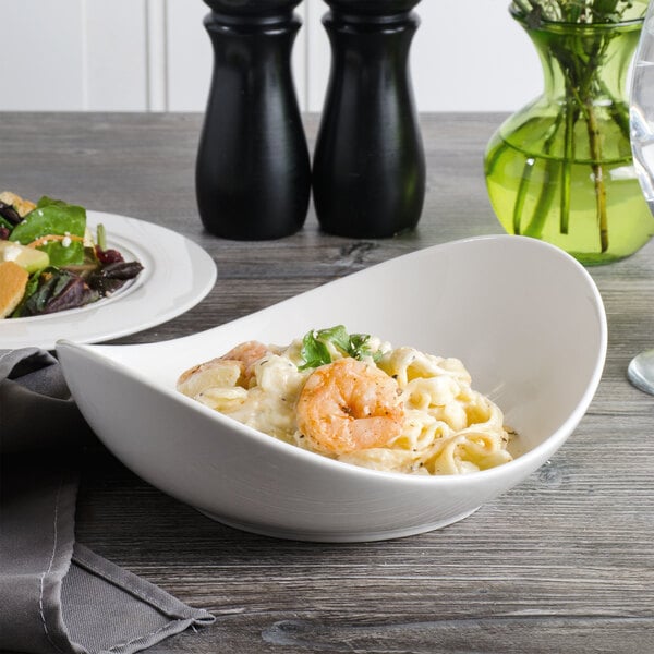 A white porcelain pasta bowl filled with shrimp and pasta on a table.