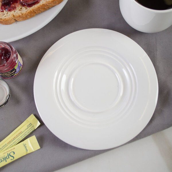 A white porcelain saucer with a cup of coffee and a jar of jam on a table.