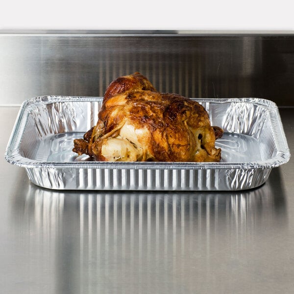 A cooked chicken in a Western Plastics shallow foil tray on a counter.