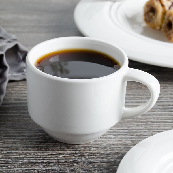A Bon Chef white porcelain espresso cup filled with coffee sits on a table next to pastries.
