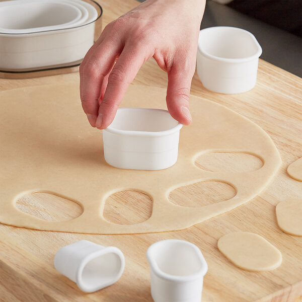 A person using Ateco oval pastry cutters to cut dough on a wooden surface.