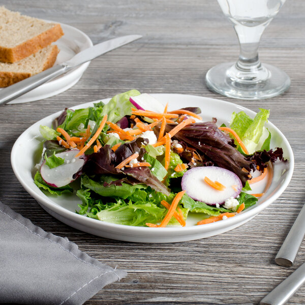 A Bon Chef white porcelain plate with a salad, bread, and knife.