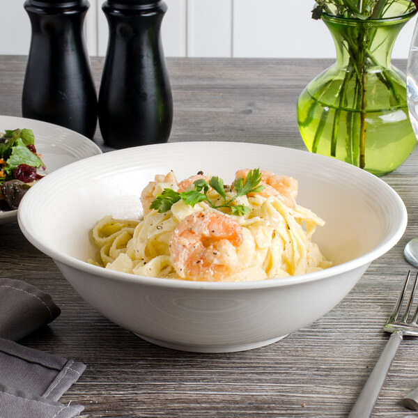 A white porcelain bowl filled with pasta, shrimp, and vegetables.