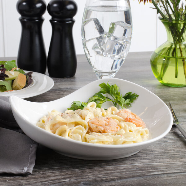 A Bon Chef white porcelain pasta bowl filled with pasta, shrimp, and vegetables on a table.