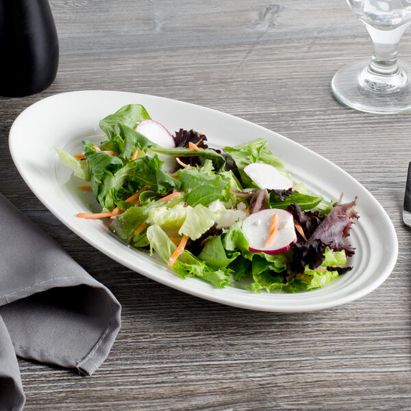 A Bon Chef white porcelain slanted oval plate with a salad on a table.