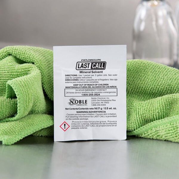 A green towel with a white label on a white paper packet with black text.