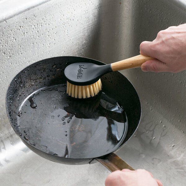 A person cleaning a pan with a Lodge scrub brush.