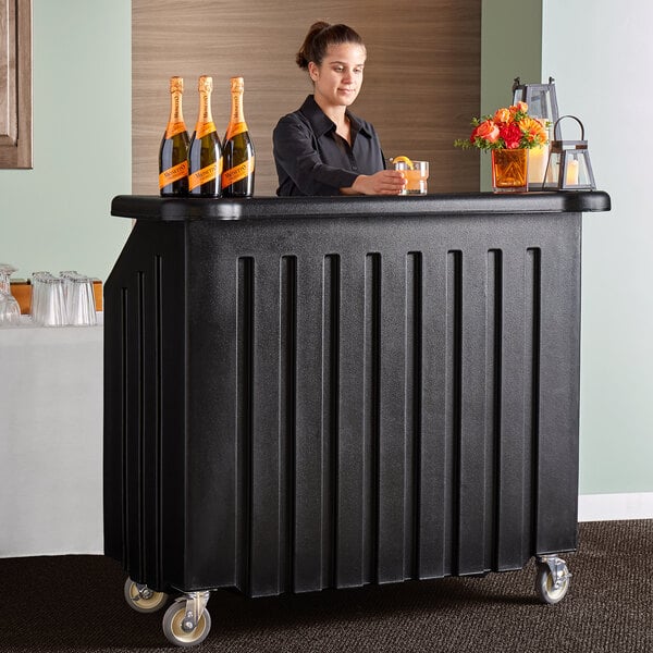 A woman standing behind a black Cambro portable bar with drinks.