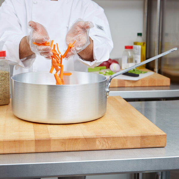 A chef putting carrots in a Vollrath aluminum sauce pan.